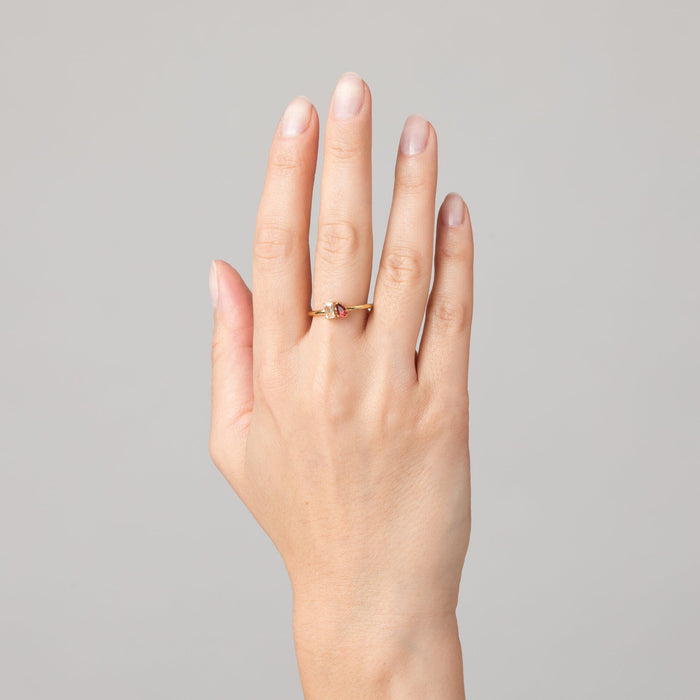Model Close-up of a woman's hand wearing a gold two-stone ring with a clear and a pink gemstone.