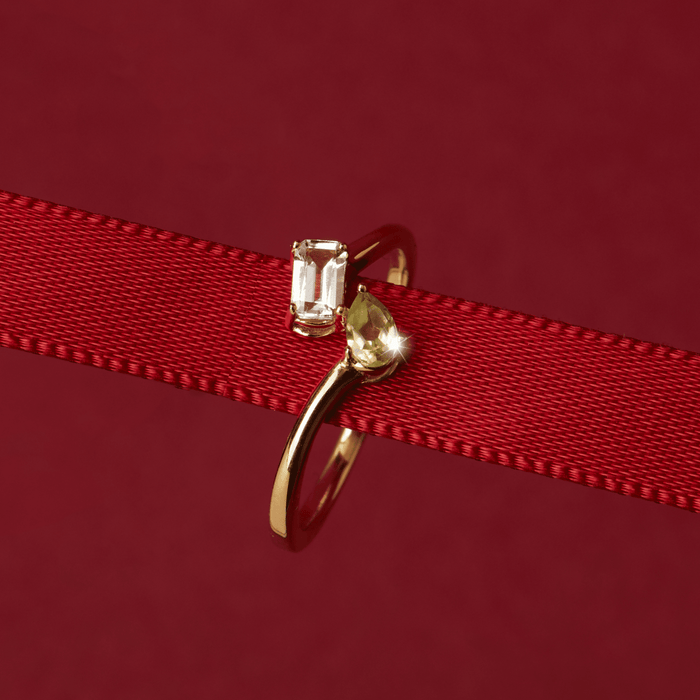 Flatlay Model Close-up of a gold two-stone ring with a clear and a yellow gemstone resting on a red ribbon.