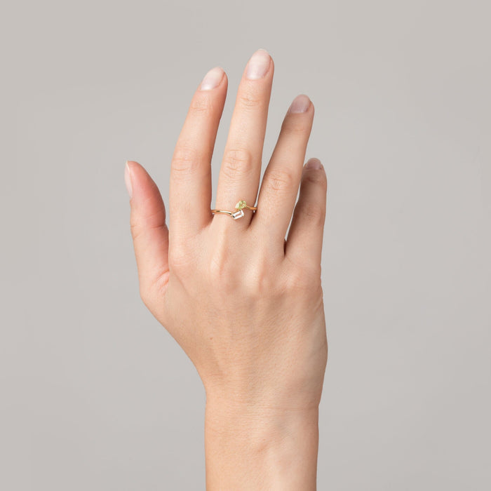 Model Close-up of a woman's hand wearing a gold two-stone ring with a yellow and a clear gemstone.