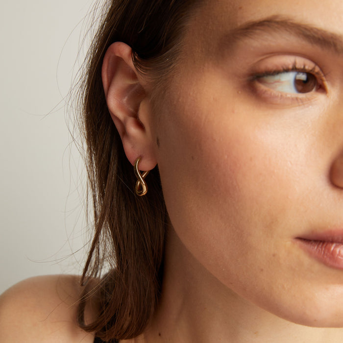 Model. Close up of a woman wearing gold twist earrings with a neutral background.