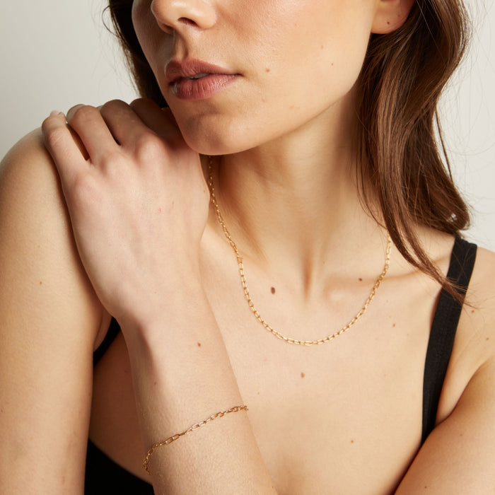 Model. Woman wearing a gold necklace and bracelet against a neutral background.
