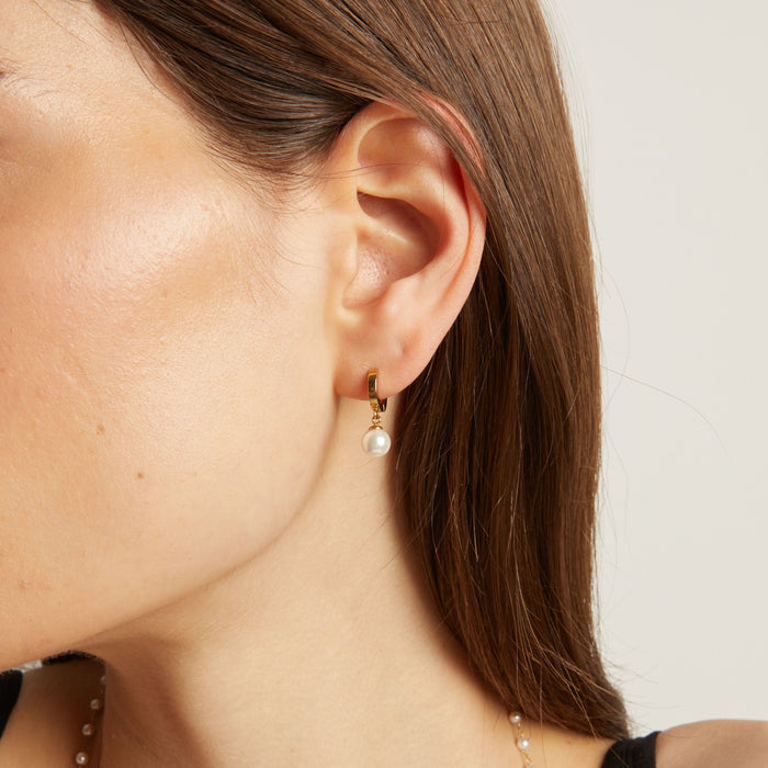 Model. Close up of a person wearing pearl earrings with a neutral background.