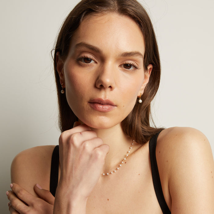 Model. Woman with pearl earring and necklace against a plain background.
