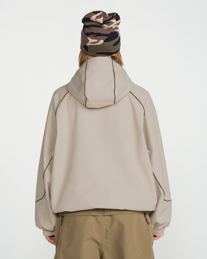 Facing away from the camera, the person is wearing the Volcom Unisex Liftline 20K Jacket in a light beige baggy fit with dark piping, paired with khaki pants and a pink, brown, and black camouflage knit beanie against a plain white background.