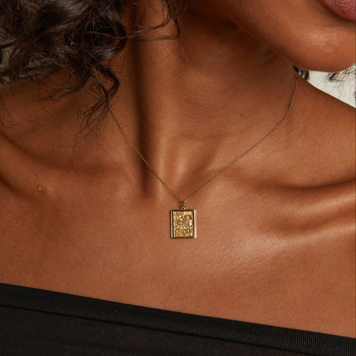 Model. Close-up of a woman wearing a gold necklace with a pendant.