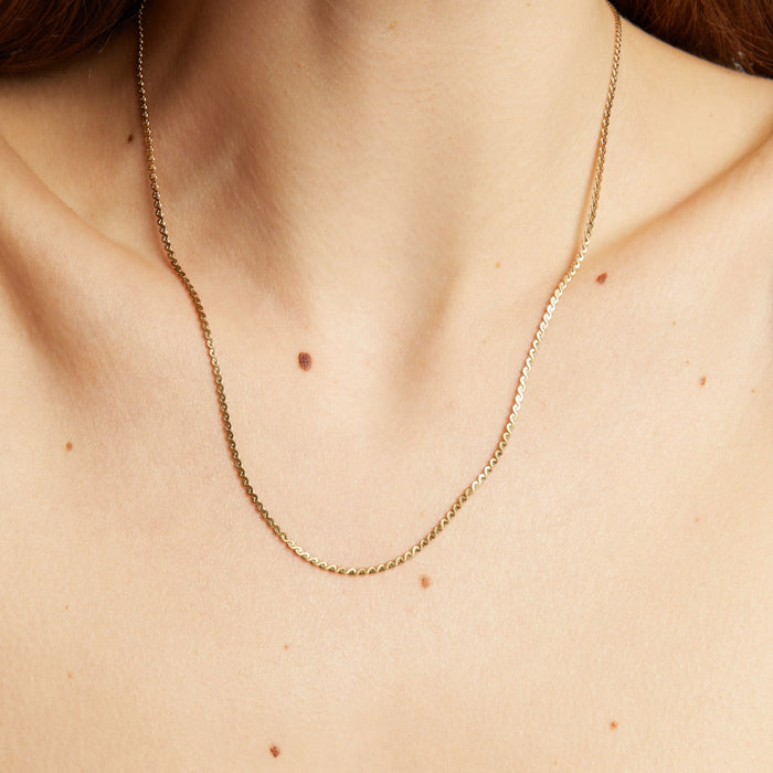 Model. Gold necklace on a person's neck with a neutral background.