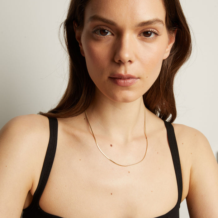 Model. Gold necklace on a woman wearing a black top against a neutral background.
