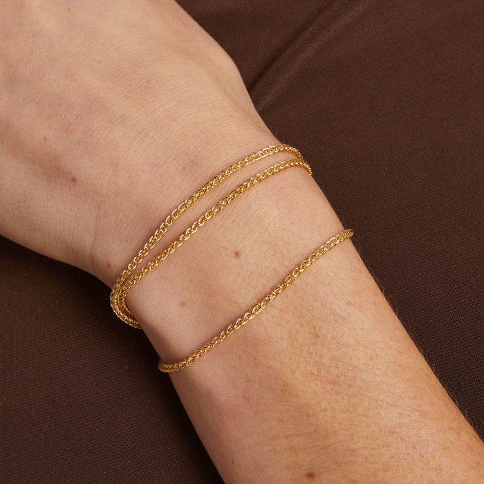 Model. Gold bracelet on a wrist against a brown background