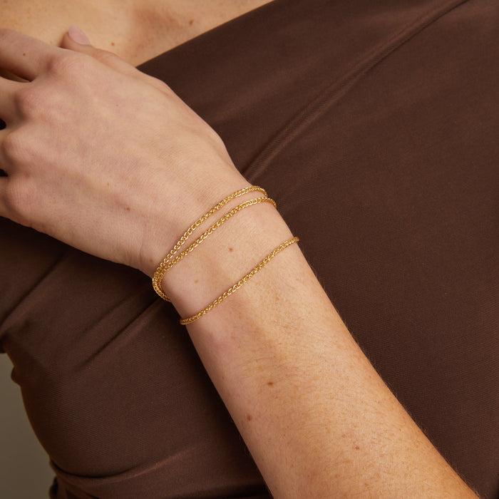 Model. Gold bracelet on a person's wrist with a plain background