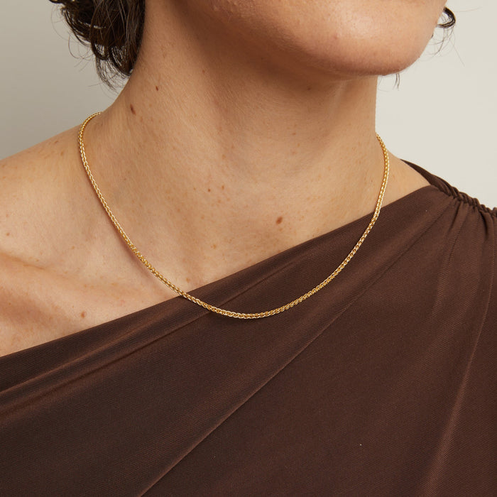 Model. Woman wearing a gold necklace and brown dress against a neutral background