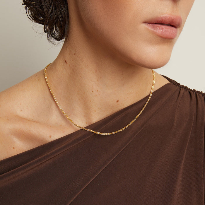 Model. Close-up of a person wearing a gold necklace with a neutral background