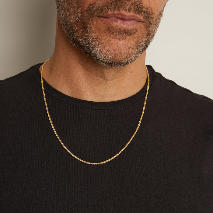 Man wearing a gold chain necklace against a neutral background