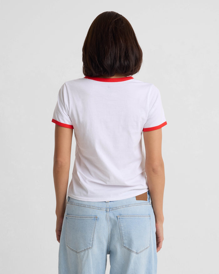 A person with medium-length brown hair, seen from behind, wears the Volcom Women's Brk Up Ringer Tee—featuring red trim on the sleeves and collar—paired with light blue jeans against a plain light background.