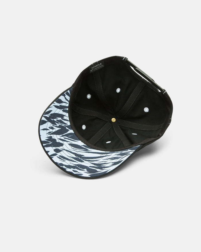 The Women's Coco Hat by Volcom is a black 5-panel cap displayed upside down, highlighting its abstract black and white patterned brim underside, mesh panels for breathability, white stitching, and a gold top button.