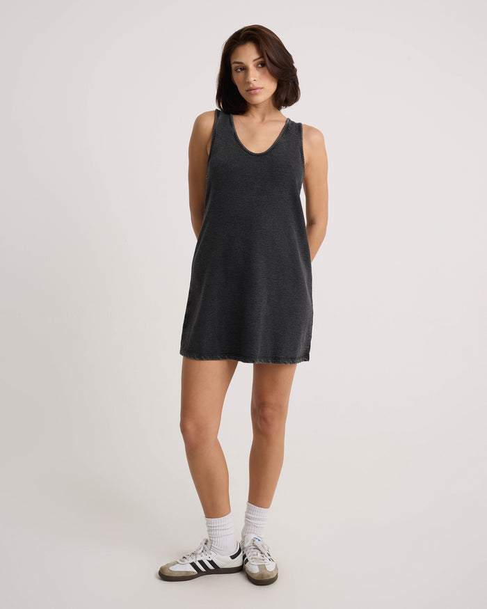 A woman with short brown hair stands against a plain white background, wearing a Volcom Women's Glam Crop Dress, white socks, and black-and-white sneakers, with her hands behind her back.
