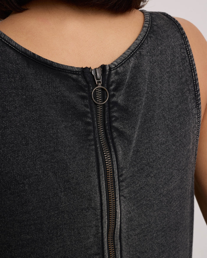 Close-up of the back of a Volcom Women's Glam Crop Dress in Vintage Black, featuring a sleeveless denim design with a metallic zipper and circular pull tab, partially unzipped, worn by a model.