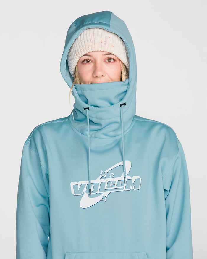 A person is pictured in a light blue Volcom Women’s Riding Hydro Pullover, featuring a high neck and drawcord hood worn up, paired with a white knit beanie. Crafted from hydrophobic fleece for added comfort and functionality, the scene is set against a plain, light-colored background.